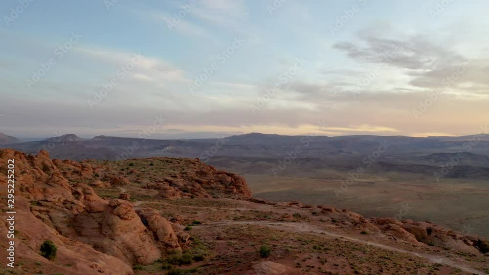 Aerial-Flying low over rugged sandstone rocks at the edge of a mesa laced with dirt roads and trails to reveal distant valley at golden hour Aerial-Flying low over rugged sandstone rocks at the edge of a mesa laced with dirt roads and trails to reveal distant valley at golden hour