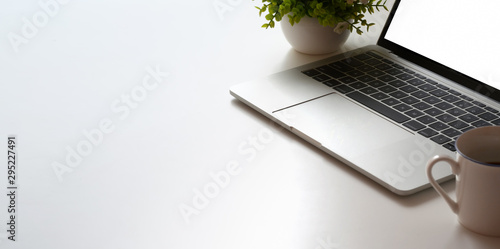 Cropped shot of minimal workspace with laptop computer and tree pot on white table table