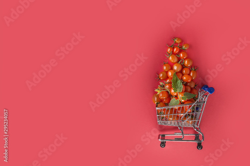 juicy tomatoes in shopping cart on red background. Copy space