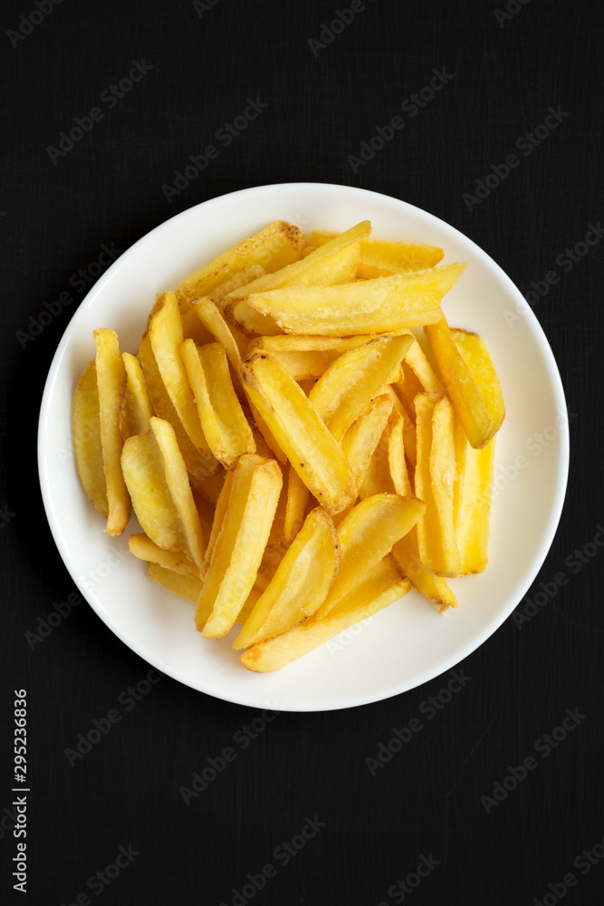Homemade french fries on a white plate on a black background, top view. Flat lay, overhead, from above. Close-up. Homemade french fries on a white plate on a black background, top view. Flat lay, overhead, from above. Close-up.