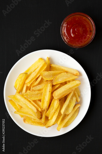 Homemade french fries with sour-sweet sauce on a white plate on a black surface, top view. Flat lay, overhead, from above.