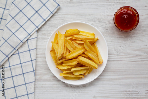 Homemade french fries with sour-sweet sauce on a white plate on a white wooden surface, top view. Flat lay, overhead, from above.