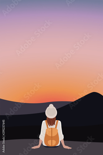 A red haired girl in a white sweater and a knitted hat with a brown backpack behind her sits on a rock and looks at the mountains and the sunset.