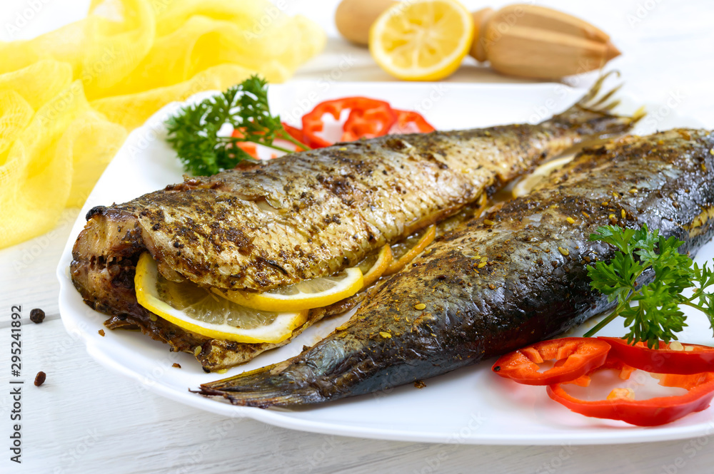 Baked herring with lemon and spices on the plate on a white wooden table. Tasty fish dish. Baked herring with lemon and spices on the plate on a white wooden table. Tasty fish dish.