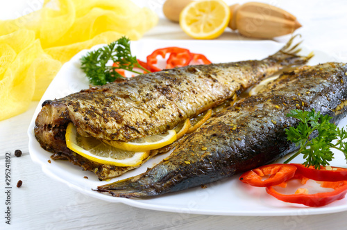 Baked herring with lemon and spices on the plate on a white wooden table. Tasty fish dish.