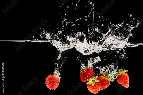 fresh ripe strawberries falling in water with splash isolated on black
