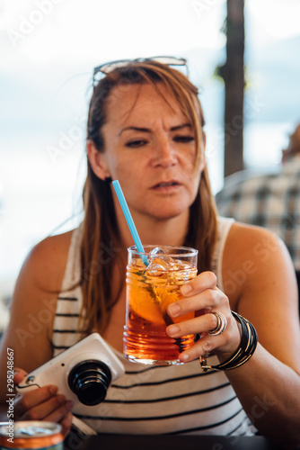une femme buvant un Aperol Spritz. Une femme boit un apéro. Une femme touriste boit un cocktail. Une touriste en vacances avec un cocktail et un appareil photo.