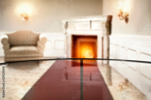 Glass table top with blurred fireplace in luxury home interior. Table background with empty space for products and decorations.