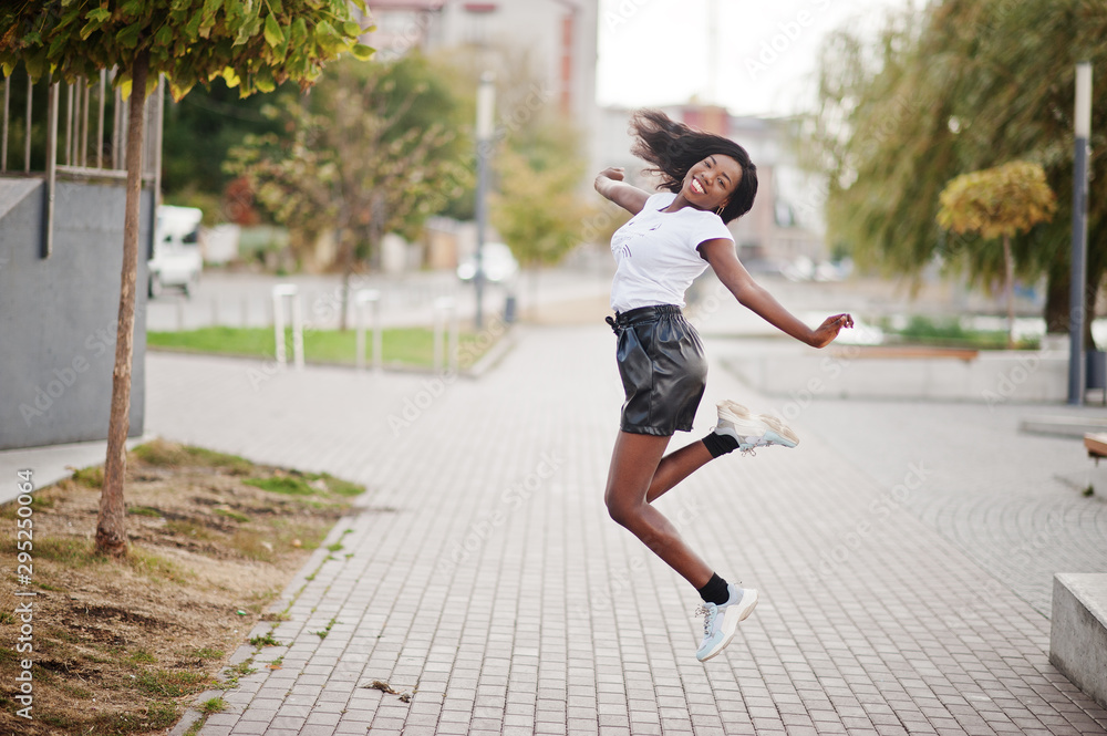 African american dark skinned slim model posed in a black leather shorts and white t-shirt. She jumping at the air. African american dark skinned slim model posed in a black leather shorts and white t-shirt. She jumping at the air.
