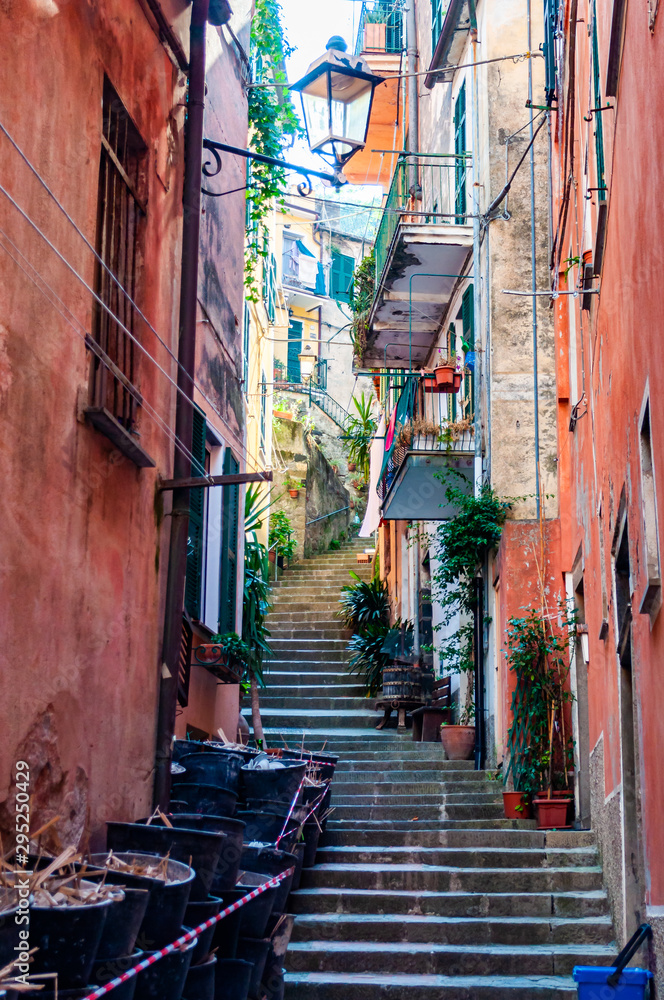 Curved elevated stairs street full of outdoor elements like street lanterns, growing plants, balconies and windows telling their stories about the city life in Monterosso Al Mare, Cinque Terre
