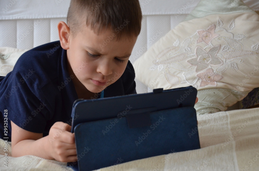 little boy at expressive face using a digital tablet in bed plays games, watch cartoons, talks with friends, writes a message little boy at expressive face using a digital tablet in bed plays games, watch cartoons, talks with friends, writes a message