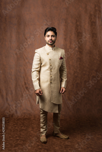 Indian bridegroom wears ethnic or traditional kurta / cloths.  Male fashion model in sherwani, posing / standing against brown grunge background, selective focus photo