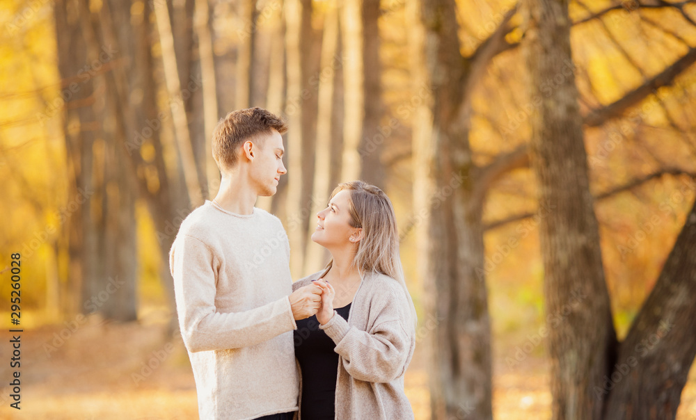 Loving couple stands embracing in autumn forest in light beige sweaters, yellow background with leaves