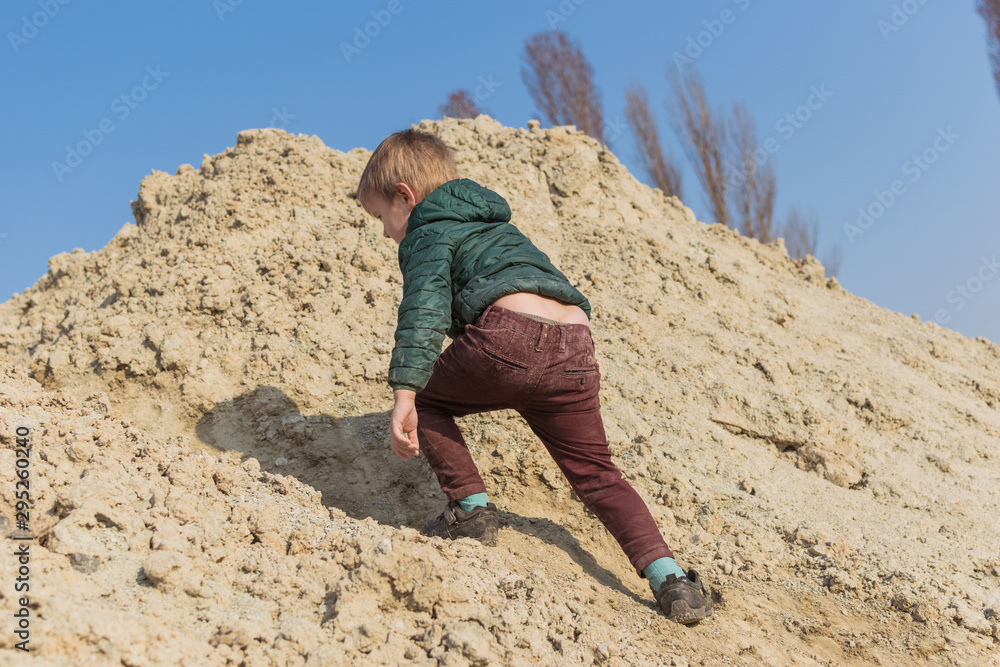 A little boy is climbing a sand mountain.