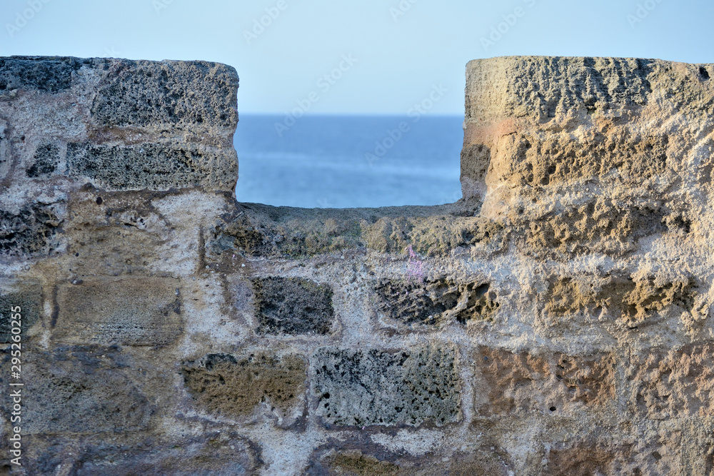 typical wall element constituting the ancient city walls of Alghero Sardinian town, illuminated by the morning sun, with the sea of ​​Sardinia in the background