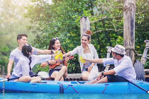 Cheerful friends together travelling, sitting at small bridge let playing ukulele guitar talking, drinking and celebrate their vacation
