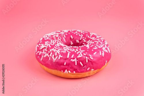 A close-up side view of one isolayed pink donut on pink background