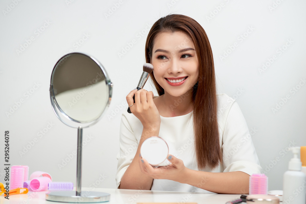 Beauty woman applying makeup. Beautiful girl looking in the mirror and applying cosmetic with a big brush. Girl gets blush on the cheekbones. Powder, rouge Beauty woman applying makeup. Beautiful girl looking in the mirror and applying cosmetic with a big brush. Girl gets blush on the cheekbones. Powder, rouge