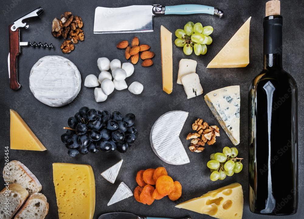Fototapeta premium different varieties of cheese with fruits, nuts, dried fruits and kitchen utensils for cheese plate. Roquefort, Maasdam, emental, Gouda, Parmesan, mozzarella and other cheeses. The view from the top