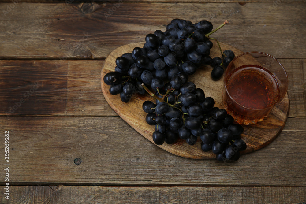 glass of cognac or wine and a juicy bunch of black grapes on a wooden rustic table