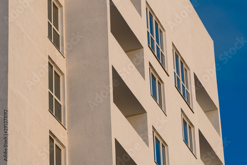 part of the white facade of the building with windows and balconies against a clear blue sky at sunrise and sunset