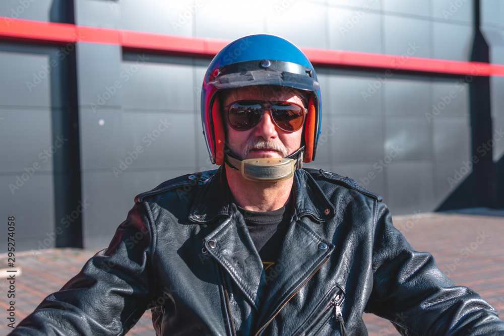 Portrait of a middle-aged man sitting at the wheel of a motorcycle, an old biker in a leather jacket on a retro bike, vintage. concept of freedom and style, a hobby for life. selective focus
