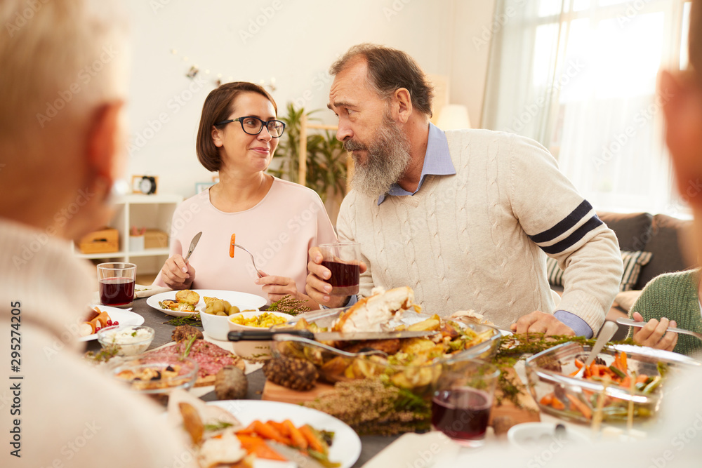 Woman and man sitting at the table eating and drinking and talking to each other during holiday dinner at home