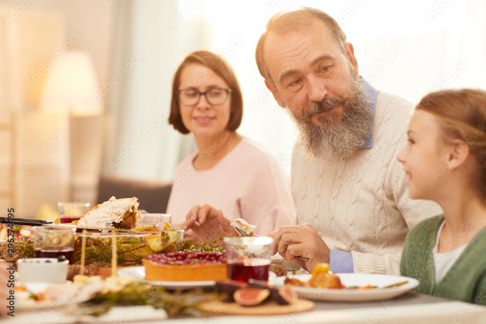Senior man with beard sitting together with little girl at the table they enjoying the meal and time together