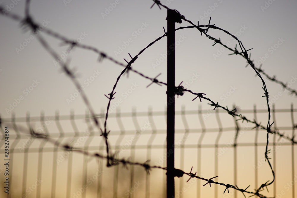 black silhouette of a barbed wire fence in summer evening, pale blue orange sky background. black silhouette of a barbed wire fence in summer evening, pale blue orange sky background.