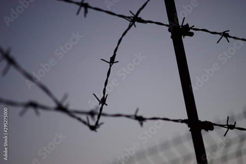 black silhouette of a barbed wire fence in evening blue sky.