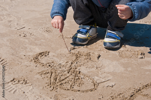 Baby draws on the sand with a wooden stick on a winter day. Children's games. Winter dressed child on the beach. photo