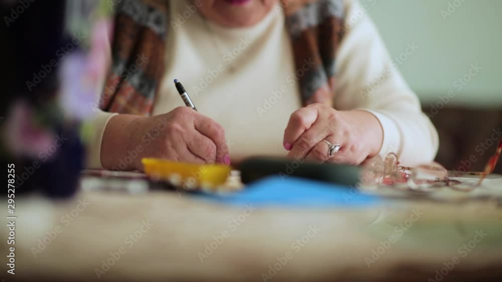 Grandma with glasses handwriting a letter to her family. Tablets for her medical condition Grandma with glasses handwriting a letter to her family. Tablets for her medical condition