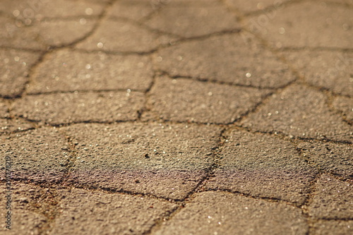 Sunny road surface made of old asphalt with cracks. Stone texture with warm sun light
