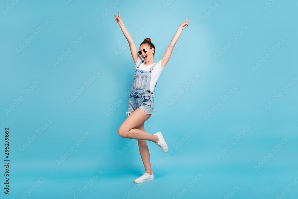 Full length body size photo of chilling dancing walking girl careless wearing jeans denim overall showing everyone v-sign while isolated with blue background