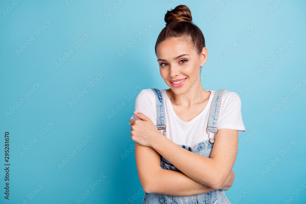 Portrait of charming youth cuddling herself wearing white t-shirt denim jeans overall isolated over blue background Portrait of charming youth cuddling herself wearing white t-shirt denim jeans overall isolated over blue background