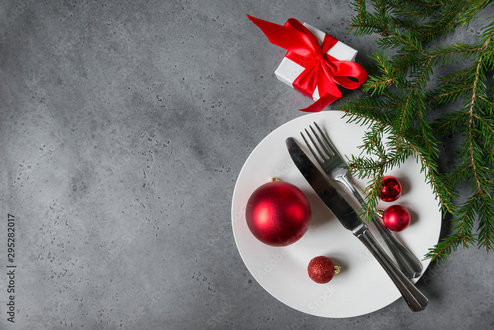fork and knife, red Christmas balls of different sizes on a white plate, spruce branch on a gray background, Christmas serving fork and knife, red Christmas balls of different sizes on a white plate, spruce branch on a gray background, Christmas serving