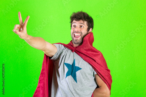 Young crazy super hero making a victory gesture, feeling happy, positive and successful over green background