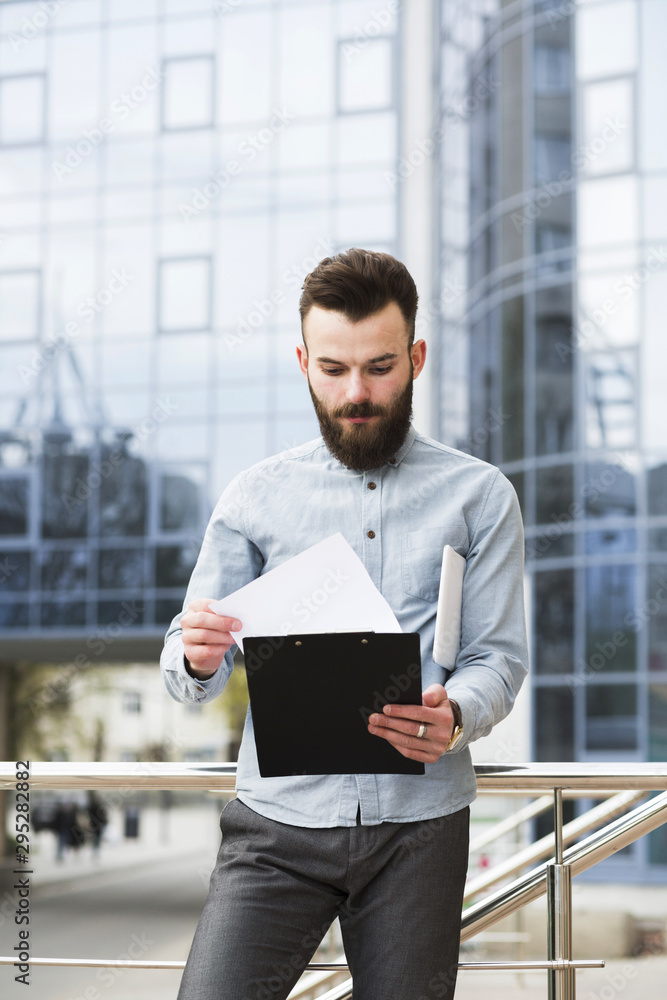Portrait of a young businessman checking the document in front of office building Portrait of a young businessman checking the document in front of office building