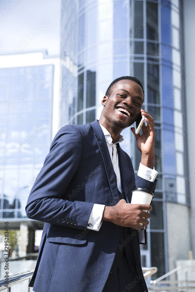 Smiling african young businessman in front of corporate building talking on mobile phone Smiling african young businessman in front of corporate building talking on mobile phone