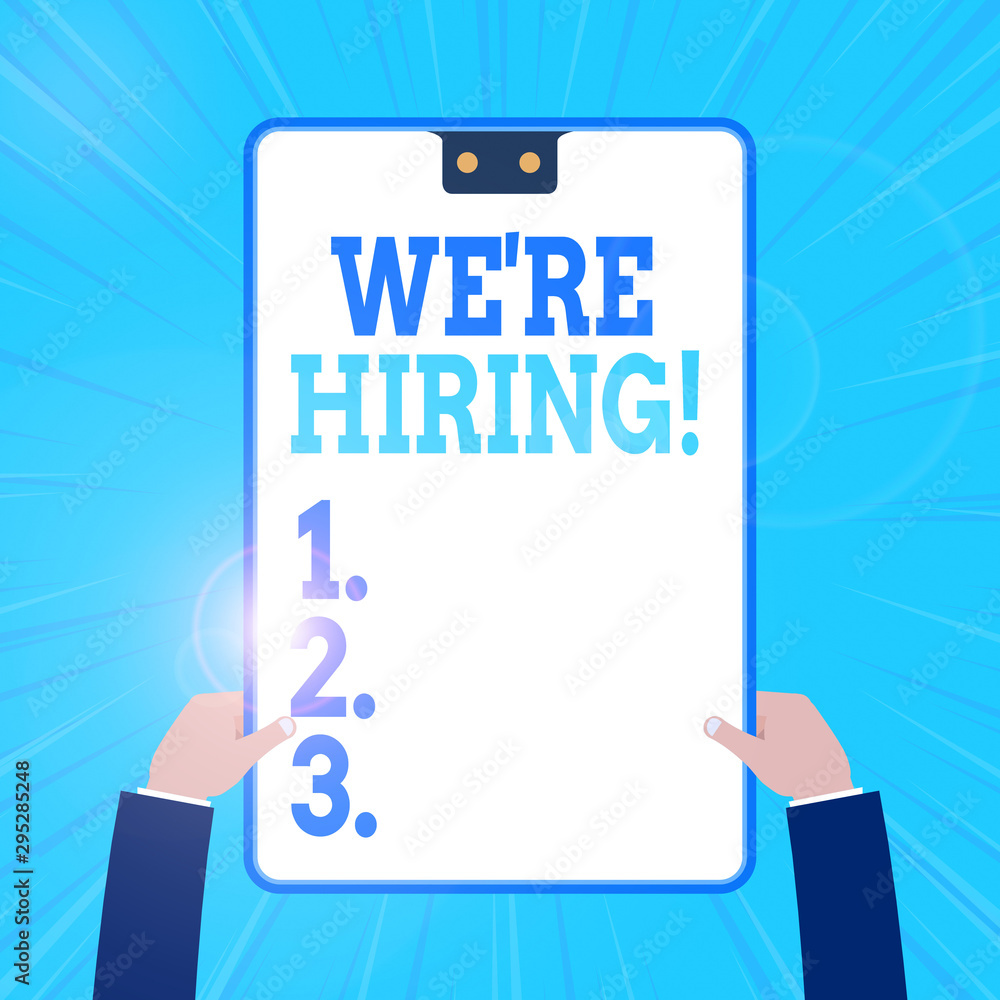 Conceptual hand writing showing We Re Hiring. Concept meaning recently employ someone or pay someone to do particular job Two male hands holding electronic device geometrical background Conceptual hand writing showing We Re Hiring. Concept meaning recently employ someone or pay someone to do particular job Two male hands holding electronic device geometrical background