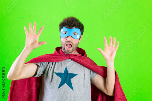 Young crazy super hero feeling excited  happy  surprised or shocked  astonished at something unbelievable over green background