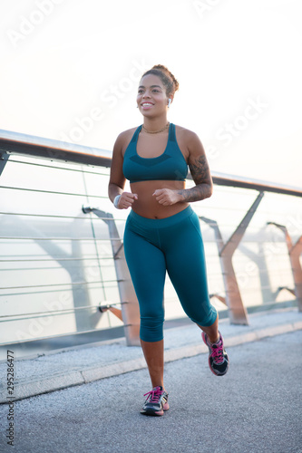 Dark-skinned young woman smiling while jogging in the morning