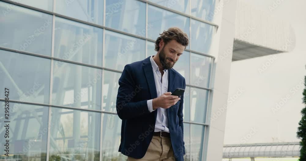 Happy Startup Businessman is surfing in Social Network on his Smartphone. Handsome Man is stylish clothed in Smart-casual Suit. Curly Hair. Business Life. Modern Office Building. Happy Startup Businessman is surfing in Social Network on his Smartphone. Handsome Man is stylish clothed in Smart-casual Suit. Curly Hair. Business Life. Modern Office Building.