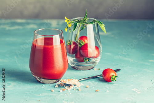 Glasses of fresh delicious jummy red tomato juice and fresh raw tomatoes with pink salt in spoon on light concrete surface. Close up. Gmo free. Natural good food photo