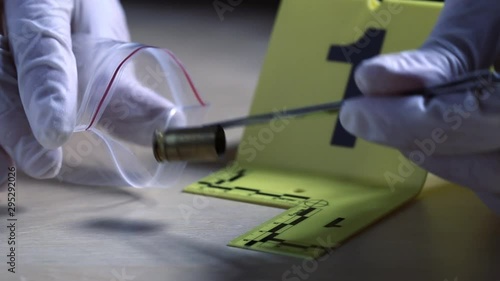 Macro shot of forensic csi police officer collecting bullet casing as evidence and putting it into plastic evidence bag on crime scene