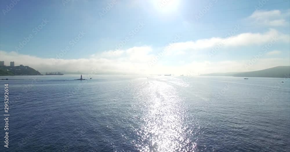 Flying above shiny water of amazing Amur bay under bright summer sun. Aerial. Tokarevsky lighthouse is on the left. Vladivostok, Russia Flying above shiny water of amazing Amur bay under bright summer sun. Aerial. Tokarevsky lighthouse is on the left. Vladivostok, Russia