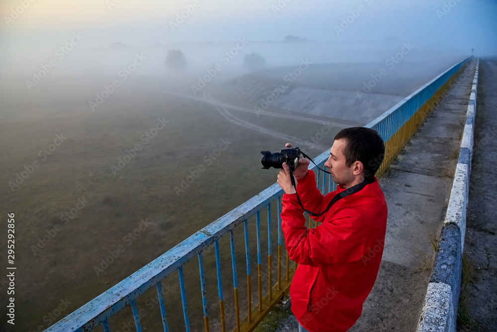 Obraz premium A man on a bridge over the river that photographs a sunrise on a foggy morning.