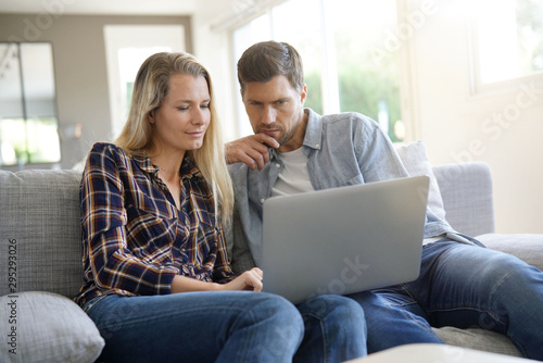 Cheerful couple at home using laptop