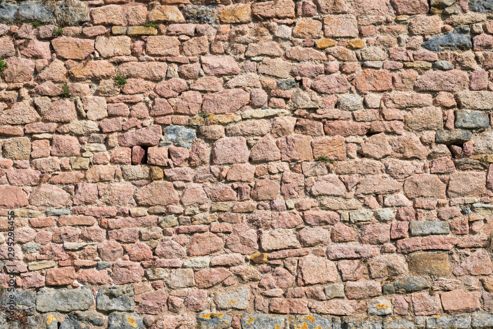 Fragment of the fortress wall of pink stones. Stones of various shapes are carefully adjusted to each other. Semur-en-Osua. Burgundy. France. Texture. Background. Fragment of the fortress wall of pink stones. Stones of various shapes are carefully adjusted to each other. Semur-en-Osua. Burgundy. France. Texture. Background.