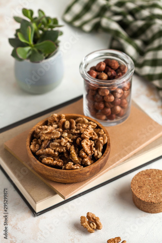 a handful of walnuts in a wooden plate, a handful of hazelnuts in a quilted jar on a light background with a green plant in the background